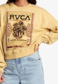 Sudadera amarilla con un diseño gráfico de flores y el texto "NATURALEZA VS INDUSTRIA". Puños y dobladillo acanalados, corte holgado.