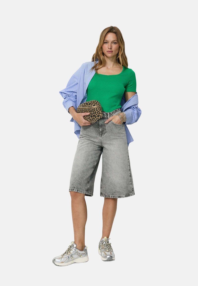 Haut moulant vert à manches courtes, superposé avec une chemise rayée bleu clair. Bermuda en denim gris, baskets argentées et pochette à imprimé léopard.