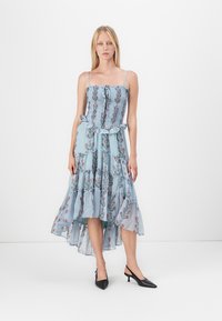 Abito blu con stampa floreale, spalline sottili, corpetto arricciato, orlo con volant e design a strati. Indossato con décolleté nere a punta.