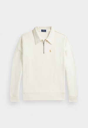 Sudadera tipo polo en color crema, con cuello de media cremallera, puños acanalados y un pequeño logo dorado en el lado izquierdo del pecho. Textura de tela suave.