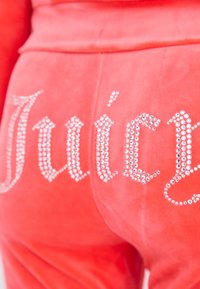 Rote Velourhosen mit dem Schriftzug "Juicy" aus Strasssteinen über dem Gesäßtaschenbereich.