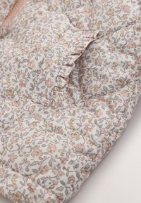 Vadderat tyg med ett pastellfärgat blommönster i rosa, beige och grått, med rynkad kant och cirkulära sömdetaljer.