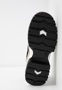 Semelle en caoutchouc noir avec des rainures profondes pour la traction, présentant une tige en suède beige. Texte imprimé sur la semelle indiquant "FABRIQUÉ EN ITALIE" et taille 37.