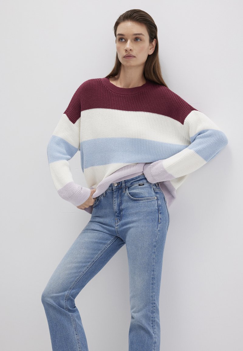 Strickpullover mit burgunderroten, weißen, hellblauen und lavendelfarbenen Streifen. Lässige Passform, gerippte Textur, kombiniert mit hoch taillierten blauen Jeans.