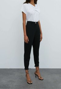Top blanco de manga corta con detalle retorcido, combinado con pantalones negros de tiro alto y ajuste ceñido, con lazos en los tobillos. Tacones negros de tiras.