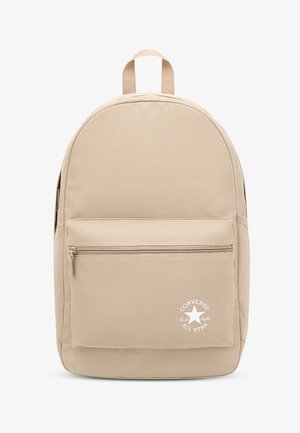 Rucsac bej cu formă rotunjită, confecționat dintr-un material neted. Are un buzunar frontal cu fermoar, logo și o mânere de sus. Design și textură simple.