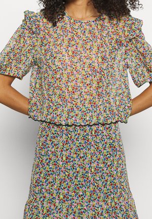 Donna che indossa una blusa e una gonna a fantasia floreale colorata, con maniche corte a sbuffo e orli svasati.