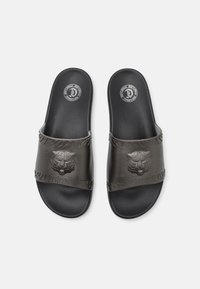Czarne klapki z teksturowanym paskiem, wyraźnym logo lwa oraz kontrastującą podeszwą z gumowym bieżnikiem dla lepszej przyczepności.