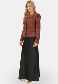 Czerwony, fakturowany żakiet z złotymi guzikami, w połączeniu z długą czarną spódnicą i złotymi butami, zaprezentowany na jednolitym białym tle.