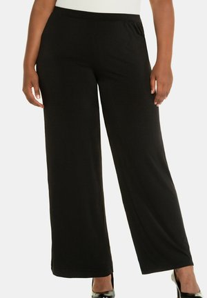 Pantalons larges noirs avec une texture lisse, dotés d'une taille élastique et d'une silhouette fluide, conçus pour le confort et la liberté de mouvement.