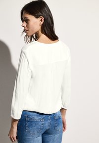 Witte blouse met lange mouwen van textuurstof en een afgeronde halslijn aan de achterkant, gecombineerd met strakke blauwe denim jeans met achterzakken.