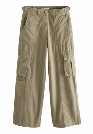 Personne portant un pantalon cargo beige, une chemise blanche boutonnée, des sandales blanches et portant un sac bandoulière tissé beige et noir.