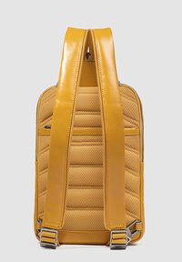 Mochila amarilla hecha de tela resistente y cuero suave, con textura acolchada, compartimentos con cremallera y correas ajustables.