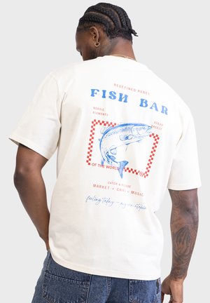 Short-sleeve cream t-shirt featuring a blue fish graphic and red text on the back, with a boxy fit and soft cotton material.