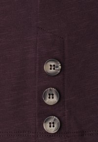 Trois boutons marbrés cousus sur un tissu côtelé violet foncé avec des coutures visibles le long des bords.