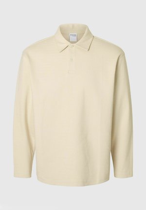 Light yellow long-sleeve polo shirt with a textured pattern, buttoned collar, and a tag visible at the neckline. Features a relaxed fit.