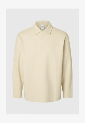 Light yellow long-sleeve polo shirt with a textured pattern, buttoned collar, and a tag visible at the neckline. Features a relaxed fit.