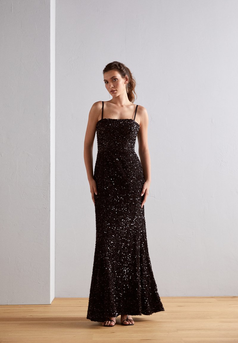 Abito da sera nero con paillettes, spalline sottili, silhouette aderente e orlo svasato. Superficie texturizzata che cattura la luce, mettendo in evidenza dettagli scintillanti.