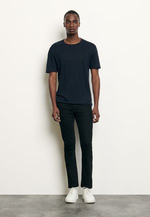 Marinblå kortärmad t-shirt i kombination med svarta slim-fit byxor och vita sneakers. Slätt tyg, rundad halsringning och avslappnad passform.