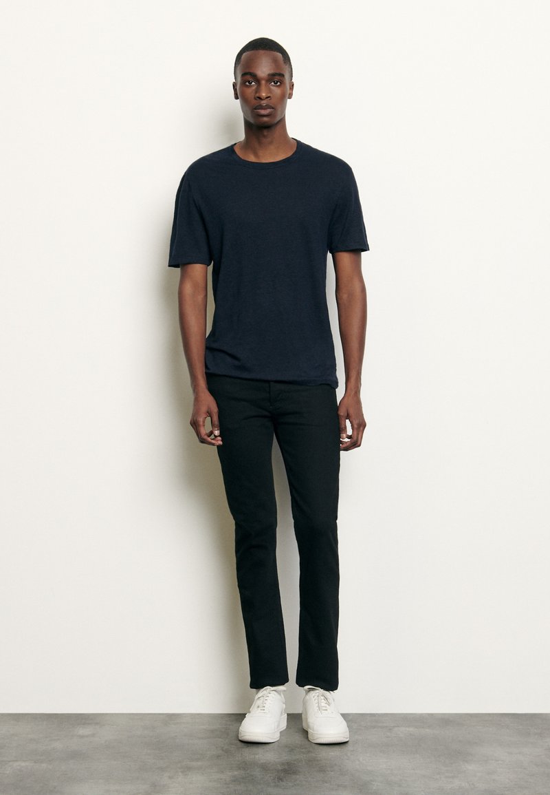Tricou cu mânecă scurtă de culoare bleumarin, asortat cu pantaloni negri skinny și adidași albi. Țesătură fină, guler tip crew și croială lejeră.