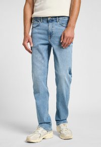 Jeans de mezclilla azul claro con corte recto, diseño de cinco bolsillos y cierre de botón de bronce, combinados con zapatillas deportivas beige.