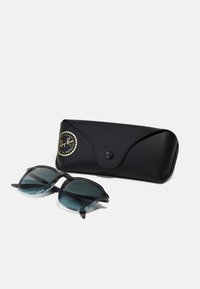Ochelari de soare Ray-Ban cu o ramă neagră, lentile gradiente albastre și accente argintii, alături de o carcasă texturată neagră cu un logo.