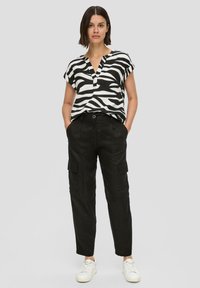 Zwart-wit gestreepte blouse met korte mouwen en een V-hals, gecombineerd met zwarte cargobroek met zijzakken en witte sneakers.