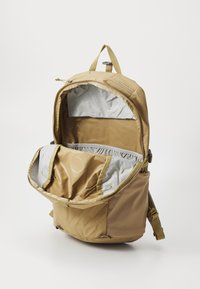Tan backpack with a spacious, silver-lined interior. Features multiple pockets and a textured exterior. Adjustable straps for comfort.
