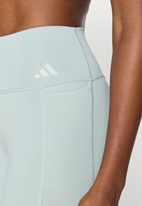 Ανοιχτό μπλε ψηλόμεσα κολάν από ελαστικό ύφασμα, με λευκό λογότυπο και ραφές flatlock για ανθεκτικότητα και άνεση.