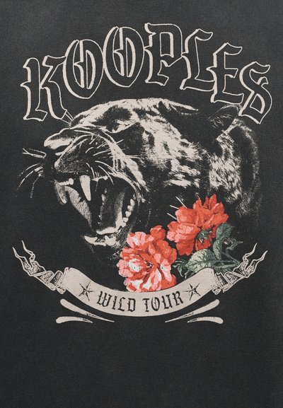 Tête de panthère rugissante avec des dents découvertes au-dessus de fleurs rouges, texte "KOOPLES" en arc au-dessus et "WILD TOUR" sur une bannière en dessous sur fond noir.