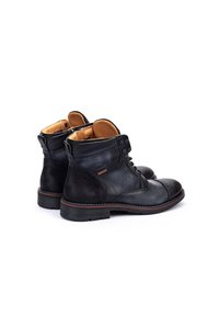 Botas de tobillo de cuero negro con puntera redondeada, panel texturizado, forro interior marrón y diseño de cordones. Presenta una suela contrastante.