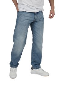 Vaaleansiniset farkut suoran lahkeen mitoituksella, kuluneen näköiset, ommeltu yksityiskohta, ja viisi taskua. Yhdistetty valkoisten lenkkarien kanssa.