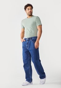 Lysegrønn kortermet t-skjorte kombinert med blå denim jeans med rett snitt og fem lommer. Hvite joggesko er brukt.