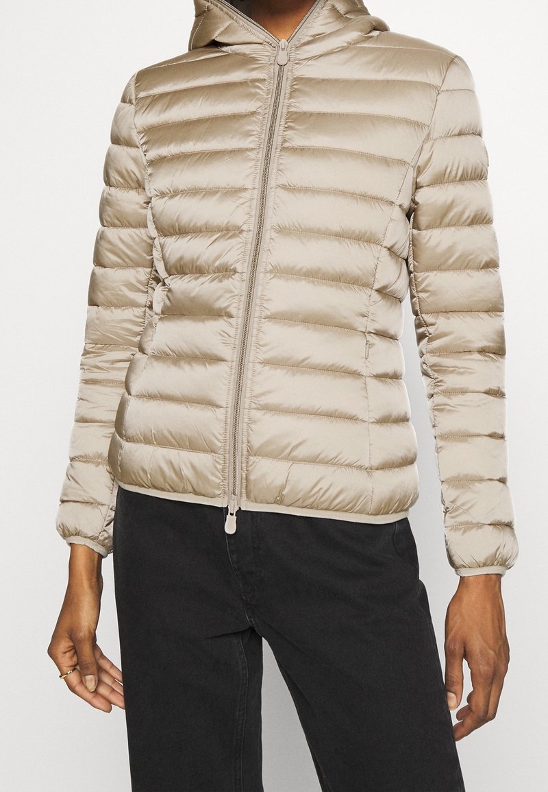 Vaaleanbeige puhvijakki, jossa on hupullinen malli, vaakasuoria tikattuja osia, etuvetoketju ja istuva helma. Pehmeä, kiiltävä kangas. 