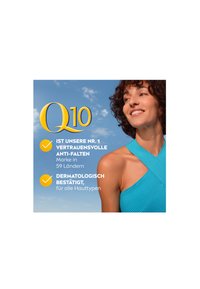 Blue sleeveless top with a textured finish. Background features a clear sky. Text highlights brand Q10 and product details in German.