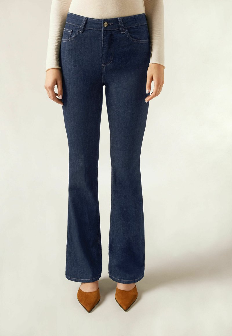 Mörkblå utsvängda jeans i denimtyg med hög midja, med framfickor och bruna klackskor med spetsig tå.