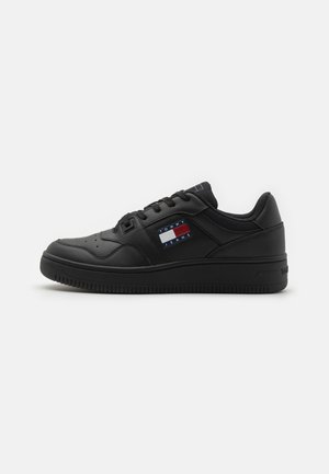 Black leather sneaker with a low profile, round toe, padded collar, and textured rubber sole. Features a logo patch in red, white, and blue.