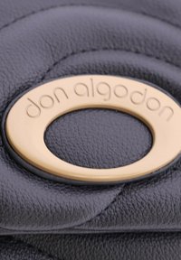 Cuero negro texturizado con un emblema circular dorado con "don algodon" grabado, destacando detalles suaves y en relieve.