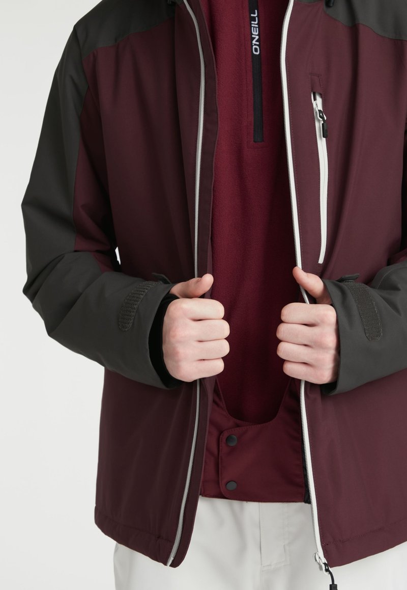 Bordeauxfarbene und schwarze Outdoor-Jacke mit einem Reißverschluss vorne, elastischen Bündchen und einem gefütterten Innenbereich, der kontrastierende Texturen und Materialien aufweist.