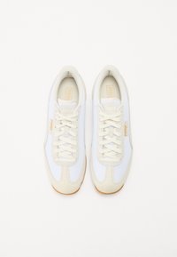 Chaussures de sport blanches en mesh et daim, bout rond, design à lacets, et semelle en caoutchouc marron clair. Aucun motif ni accent visible.