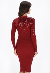 Rotes geripptes Kleid mit langen Ärmeln, das einen Farbverlauf aus Pailletten von Schwarz nach Rot auf den Schultern aufweist. Figurbetontes, knielanges Design.