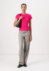 Haut rose ajusté à manches courtes, pantalon large gris et sac à épaule noir. La tenue présente une texture lisse et un design classique.