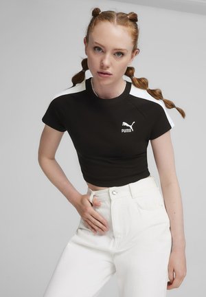 Svart kort t-shirt med korta ärmar, vita axelinslag och Puma-logotyp på framsidan, kombinerad med hög midja vita byxor.
