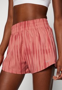 Shorts laget av lett materiale, med et rosa tie-dye mønster, elastisk midjebånd og en liten sølvfarget logo på kanten.