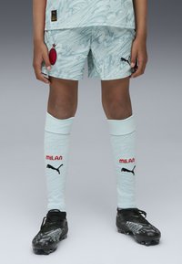 Jasnoniebieski strój piłkarski z teksturowanym wzorem, czerwone godło AC Milan, białe skarpety do kolan z napisem 'MILAN' i czarnym logo Pumy oraz czarne korki.