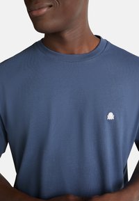 Pánské tričko s krátkým rukávem v námořnické modři, vyrobené z měkké látky, s žebrovaným kulatým výstřihem a malým bílým logem chobotnice na hrudi.