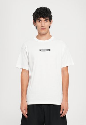 Hvit bomulls T-skjorte med rund hals og korte ermer. Har et svart rektangulært logo-patch med teksten "VERSACE JEANS COUTURE."