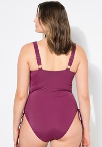 Costume intero prugna con spalline regolabili, arricciature laterali e una texture liscia. Presenta un taglio posteriore moderato per una maggiore copertura.