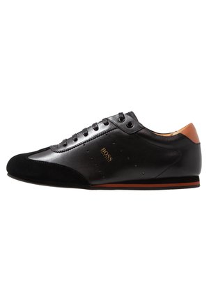 Zwarte lage leren sneaker met suède neus, bruine hielaccent, vetersluiting en gouden "BOSS" logo aan de zijkant.