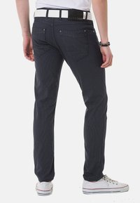 Navyblaue gemusterte Slim-Fit-Hosen mit Gesäßtaschen, kombiniert mit einem weißen Gürtel und weißen Sneakers, aus einem strukturierten Stoff.